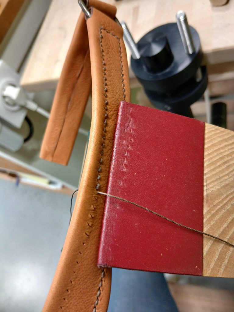 Couture manuelle au point sellier avec deux aiguilles sur une pièce de cuir maintenue dans une pince sellier